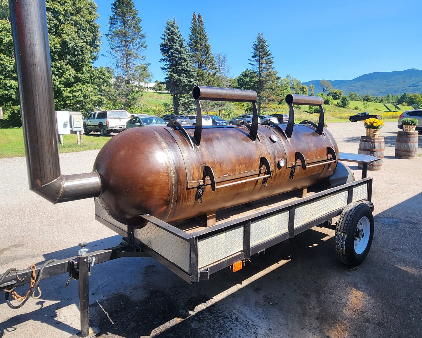 Large standard offset smoker on a trailer outdoors with trees and mountains in the background.